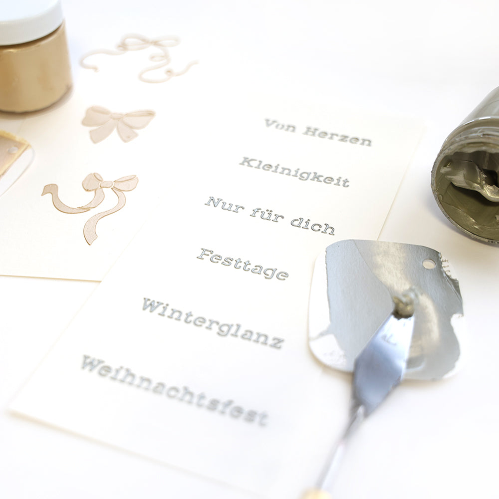 Eine Karte mit deutschen Wörtern, Metallic-Farbe, einem Spachtel und Bogenmotiven auf Weiß, hergestellt mit Alexandra Renke wiederverwendbaren Schablonen für einzigartige Schablone Papierprojekte.