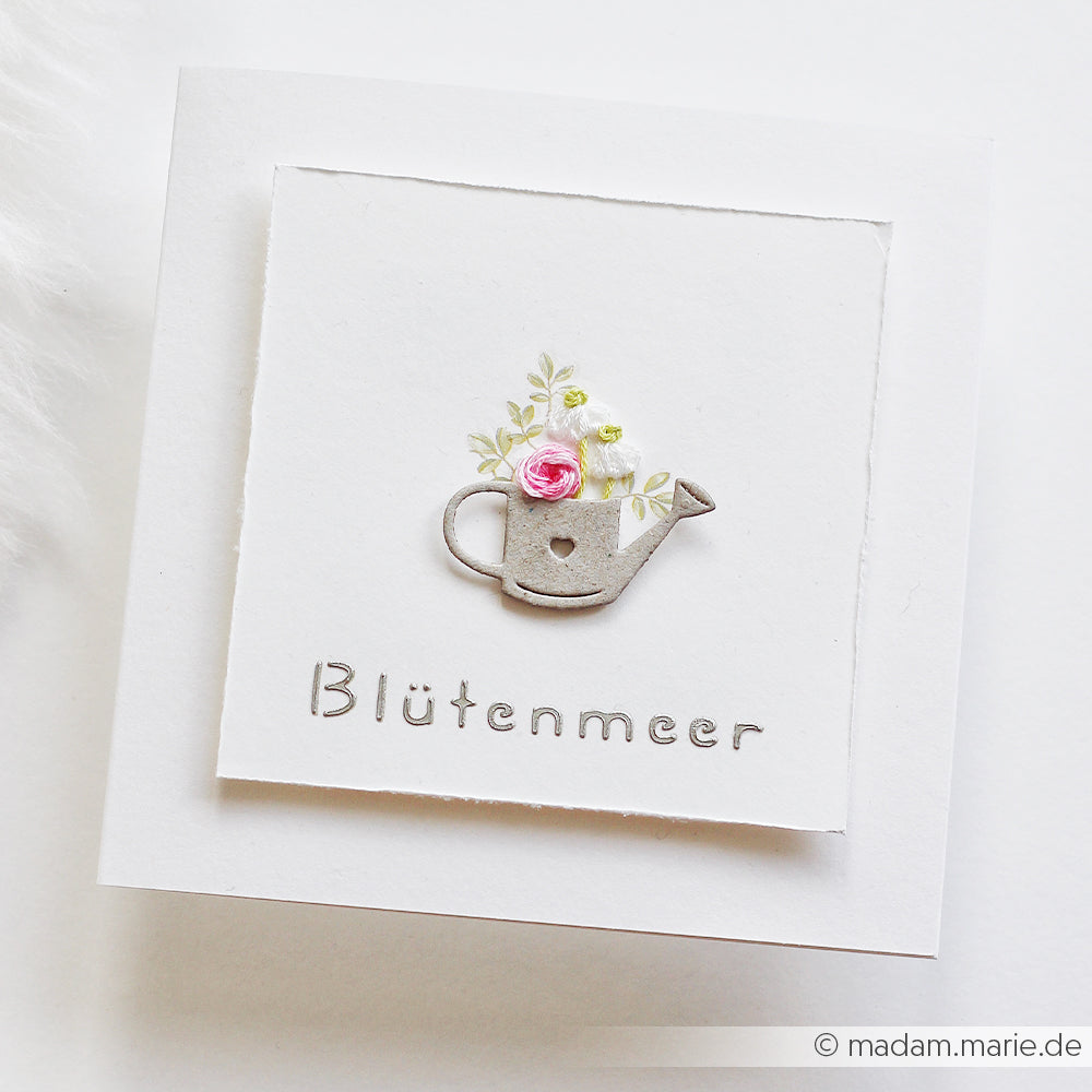 Weiße Grußkarte von Alexandra Renke mit einer kleinen Gießkanne, Blumen und dem Schriftzug „Blütenmeer“ unterhalb des Motivs – ideal zum Basteln mit wiederverwendbaren Schablonen oder als Inspiration für Ihr nächstes „Stencil Gartenzeit“-Projekt.
