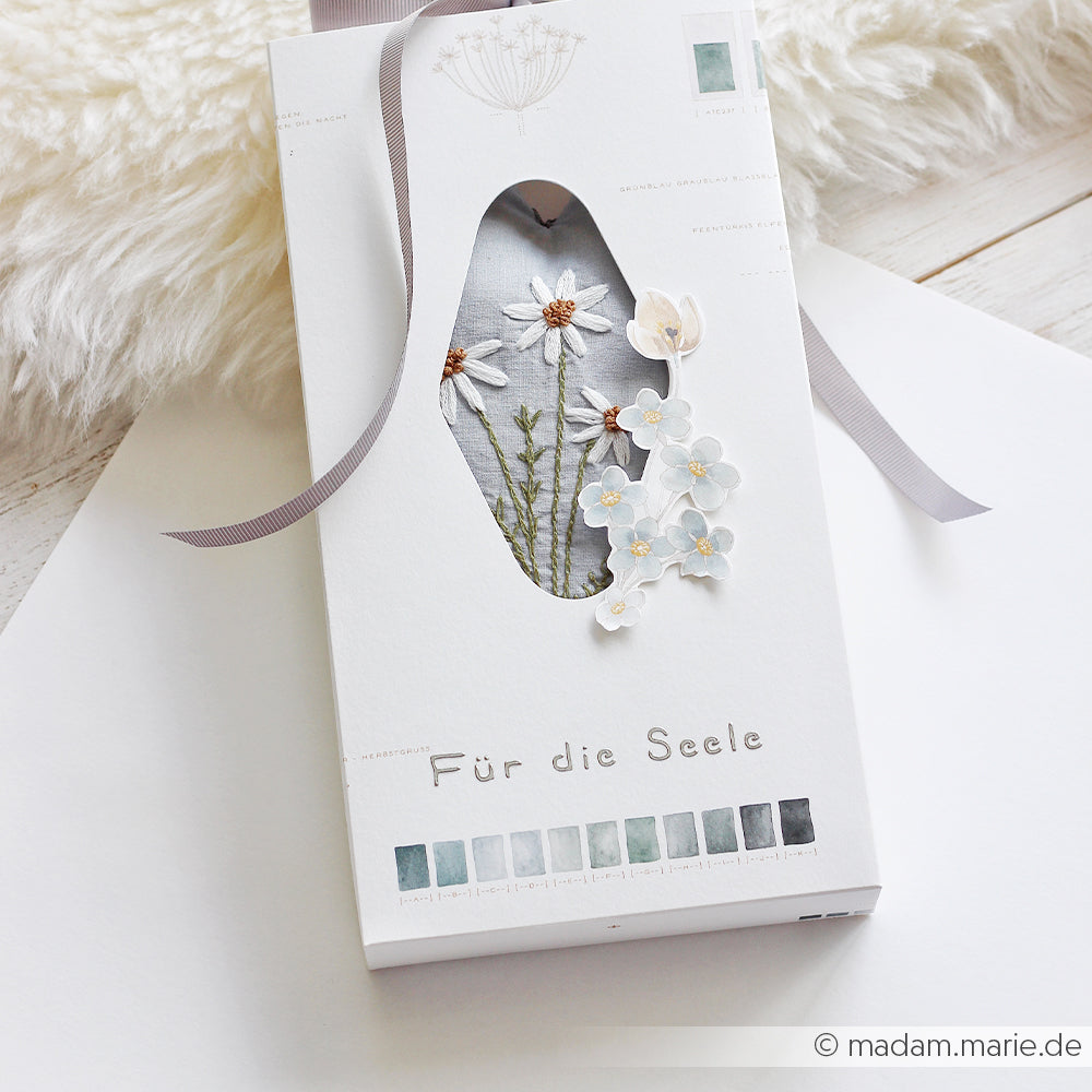 Weiße Schachtel mit Blumenstickerei und dem Schriftzug „Für die Seele“ von Alexandra Renke auf hellem Hintergrund mit Schleife – ideal für Schablonen-Papierprojekte oder zur Verwendung mit wiederverwendbaren Schablonen wie der Schablone „Kaffeeglück“.