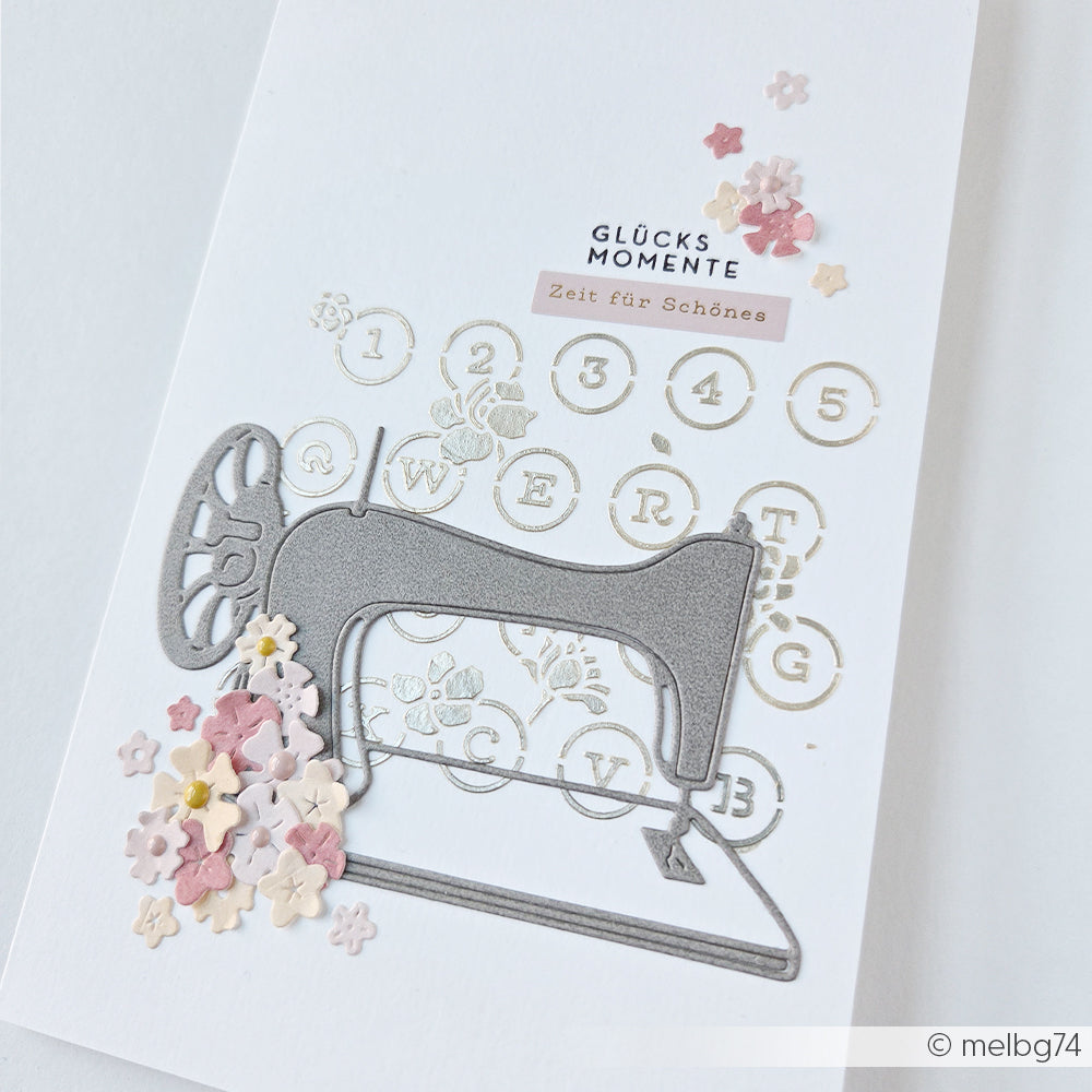 Handgefertigte Karte von Alexandra Renke mit einer silbernen Schablone mit Schreibmaschinen-Blumenmotiv, pastellfarbenen Blumen und deutschem Text auf weißem Hintergrund – ideal für Schablonen-Papierprojekte oder in Kombination mit wiederverwendbaren Schablonen.