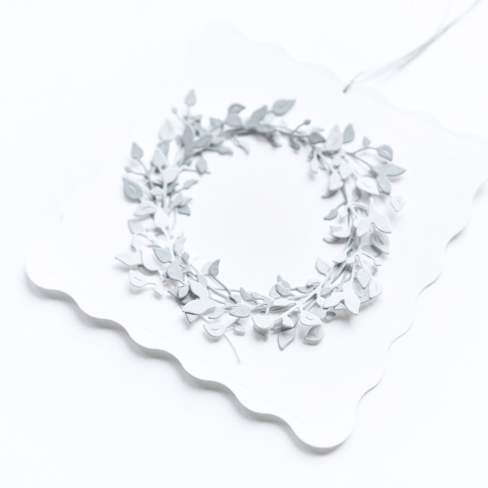 Eine weiße Karte von Alexandra Renke, gefertigt aus hochwertigen Designpapieren mit Wellenkanten und einem zarten, geprägten Silberkranz unter Verwendung der Motivstanze Blättchen Zweige Trio.