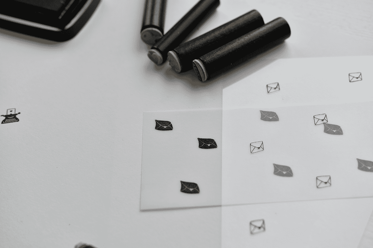 Kleine schwarz-weiße Briefumschlagstempel auf Papier und durchsichtigem Bogen, daneben Gummistempel.