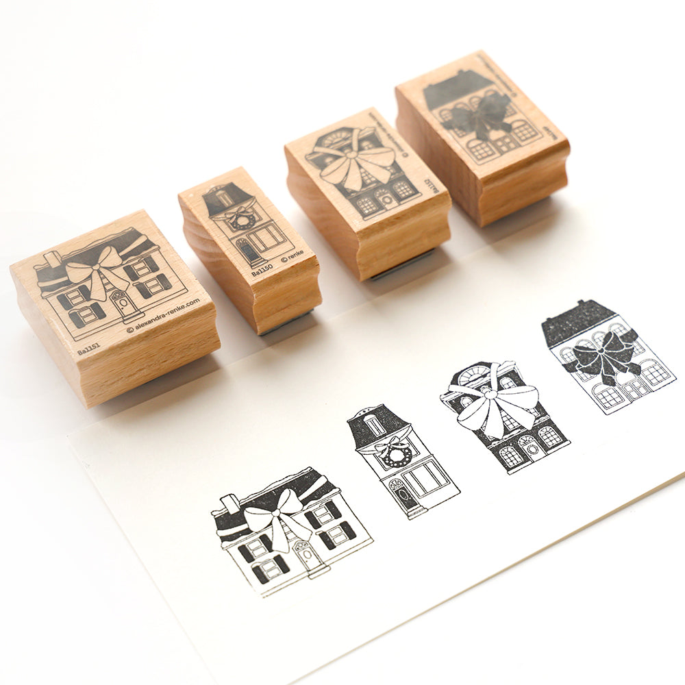 Vier Holzstempel von Häusern mit Schleifen, jeder mit einem passenden gestempelten Bild auf weißem Papier.