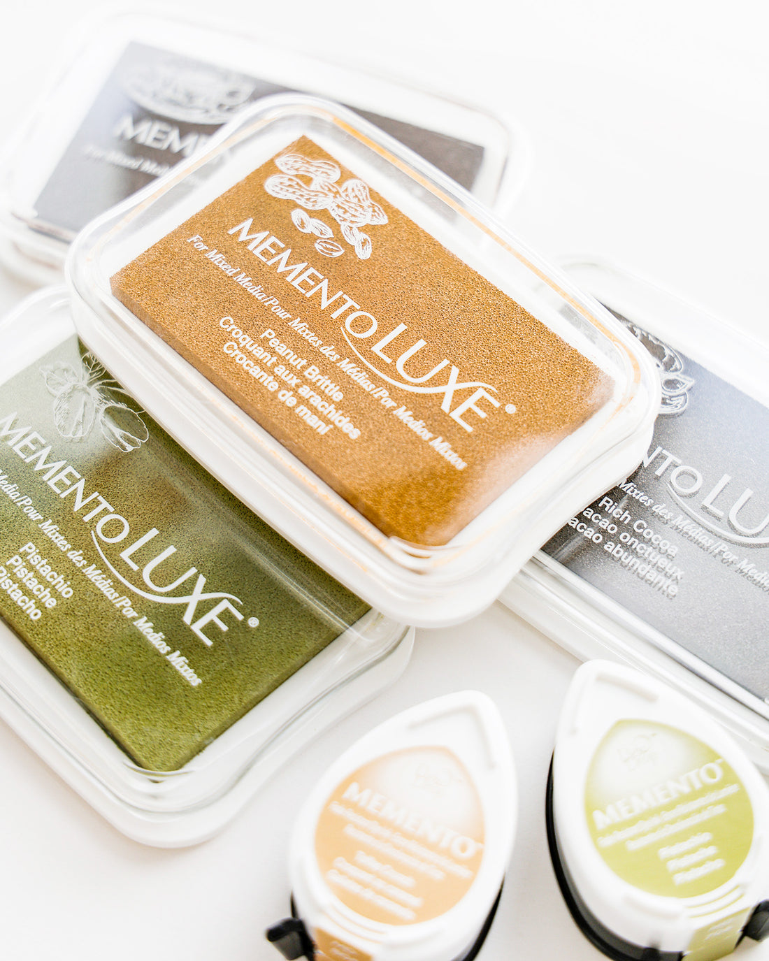 Sortierte MementoLUXE Stempelkissen in Gold, Grün und Schwarz auf weißem Hintergrund.