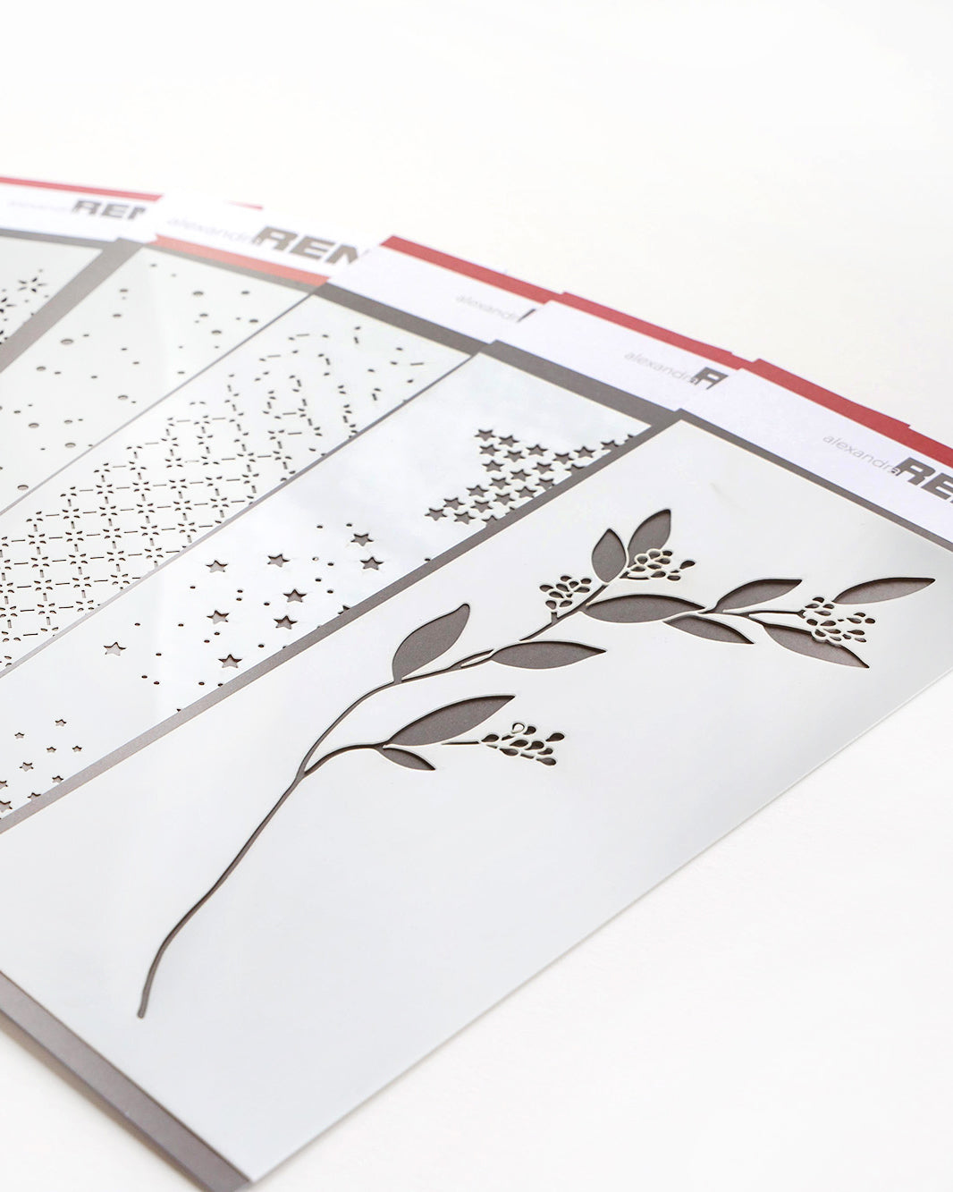 Vier dekorative Schablonen mit Mustern aus Blättern, Sternen, Punkten und Gittern, fächerförmig angeordnet.