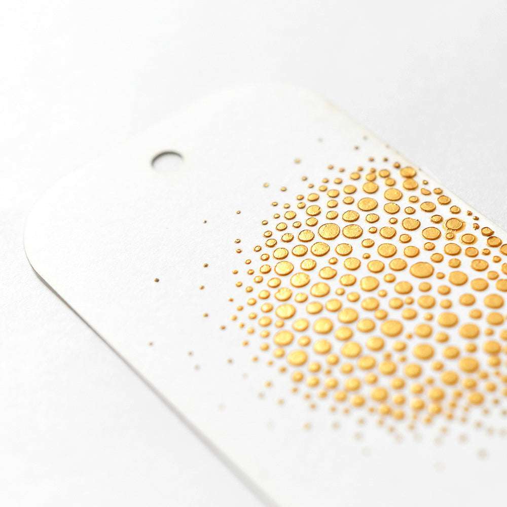 Ein weißer Anhänger von The Crafters Workshop mit erhabenen Goldfolienpunkten in einem Farbverlauf, strukturiert mit Stencil Butter und einem Loch oben - ideal für Mixed-Media-Projekte.