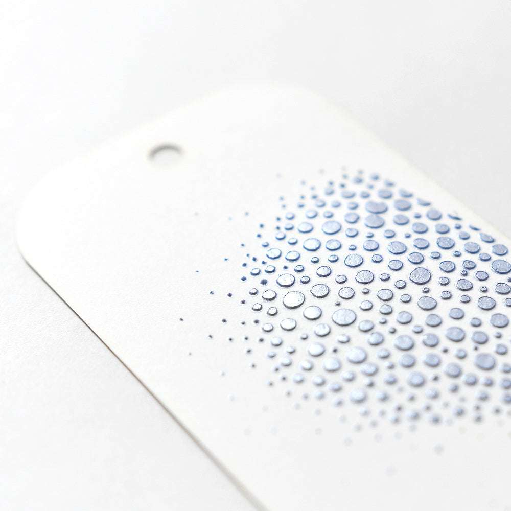 Weißer Anhänger mit Loch, mit erhabenen blauen Metallic-Punkten, die nach außen hin verblassen - ideal für Mischtechniken mit Modellierpaste oder Stencil Butter von The Crafters Workshop.