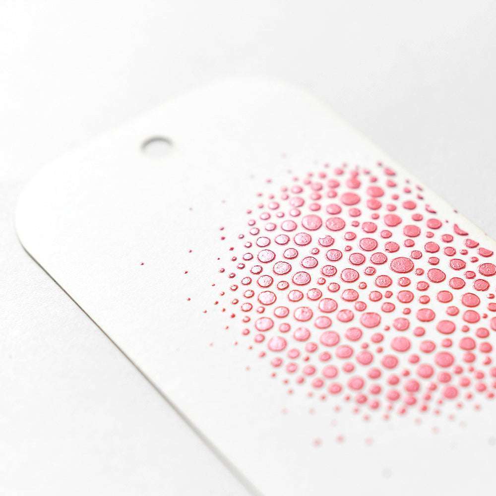 Ein weißer Anhänger mit einer Ansammlung erhabener rosafarbener Punkte in einem kreisförmigen Muster, hergestellt mit The Crafters Workshop Stencil Butter für eine glatte, dimensionale Oberfläche - ideal für Mixed Media Projekte.