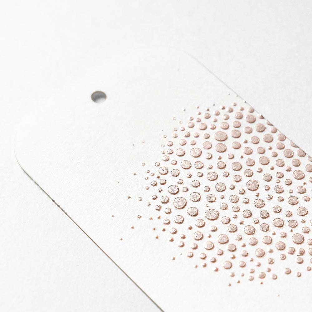 Weißer Anhänger mit Loch und geprägtem Metallic-Punktmuster in einem kreisförmigen Design auf der rechten Seite, erstellt mit Mischtechniken und The Crafters Workshop Stencil Butter für zusätzliche Textur.