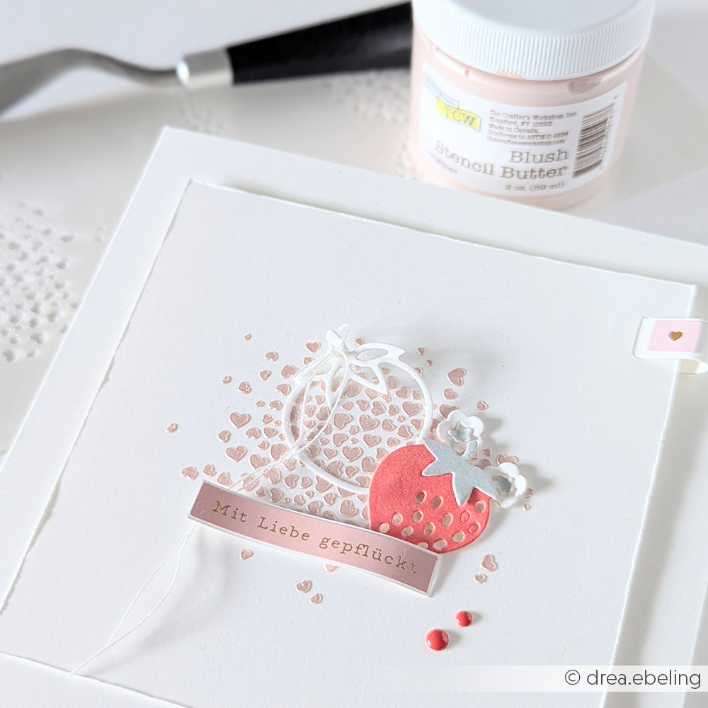 Eine handgefertigte Karte von The Crafters Workshop zeigt eine rote Erdbeere, ein Herzmuster und den deutschen Text "Mit Liebe gepflückt" auf weißem Papier, das mit zarten Mixed-Media-Techniken bearbeitet wurde.