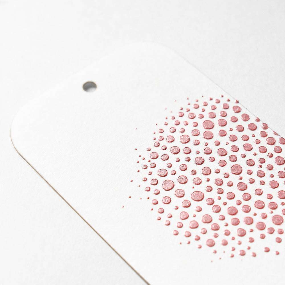 Weißer Anhänger mit einem Loch und erhabenen rosa Punkten in einem Teilkreis, hergestellt mit Modellierpaste von The Crafters Workshop - ideal für Mixed-Media-Projekte.