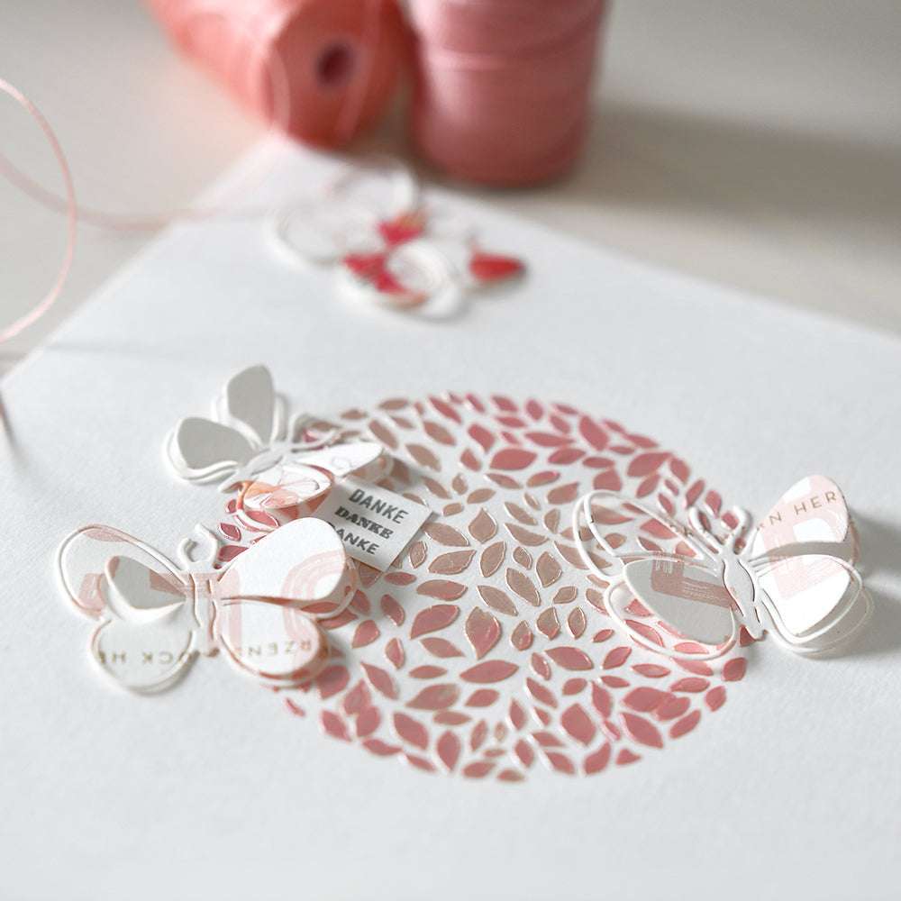 Zarte Papierschmetterlinge und ein Spitzenausschnitt auf weißem Papier, veredelt mit The Crafters Workshop schimmernde Modellierpaste und rosa Faden für einen subtilen Mixed-Media-Look.
