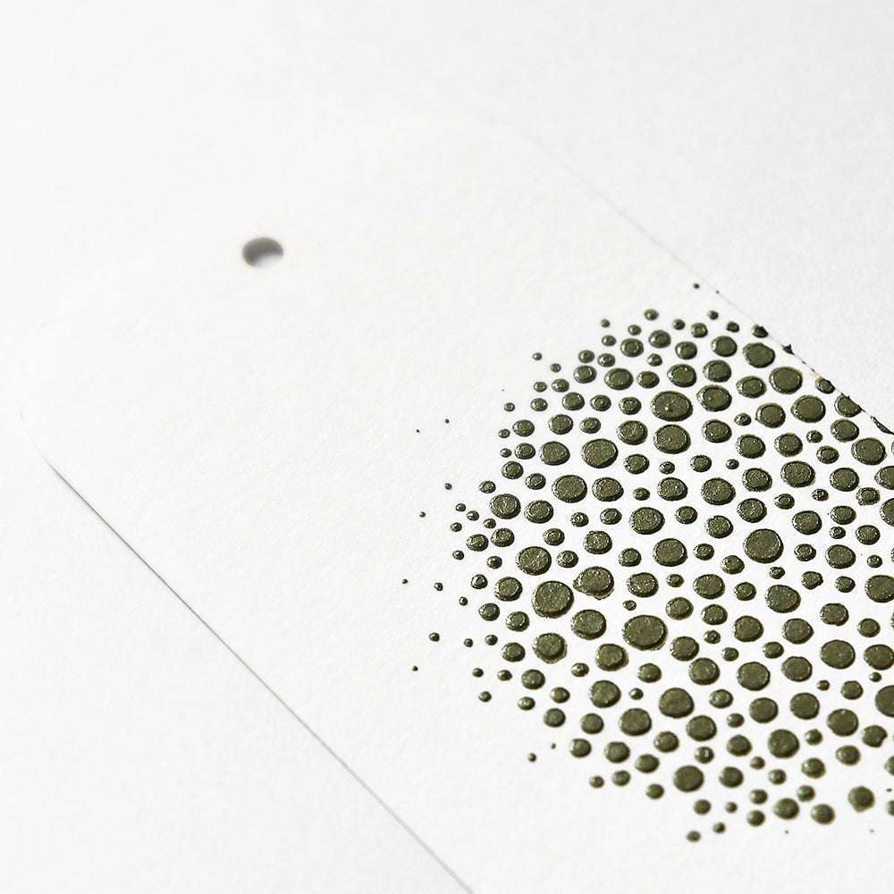 Ein weißer Anhänger von The Crafters Workshop mit einem runden Loch und einer Seite, die mit erhabenen grünen Punkten unterschiedlicher Größe verziert ist. Er wurde mit Mixed Media-Techniken und Stencil Butter-Akzenten hergestellt.