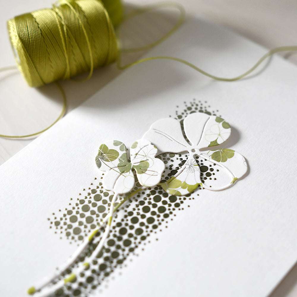 Die Mixed-Media-Karte von Crafters Workshop zeigt ausgeschnittene Blumen aus Papier und grüne Fäden auf einer weißen Oberfläche.