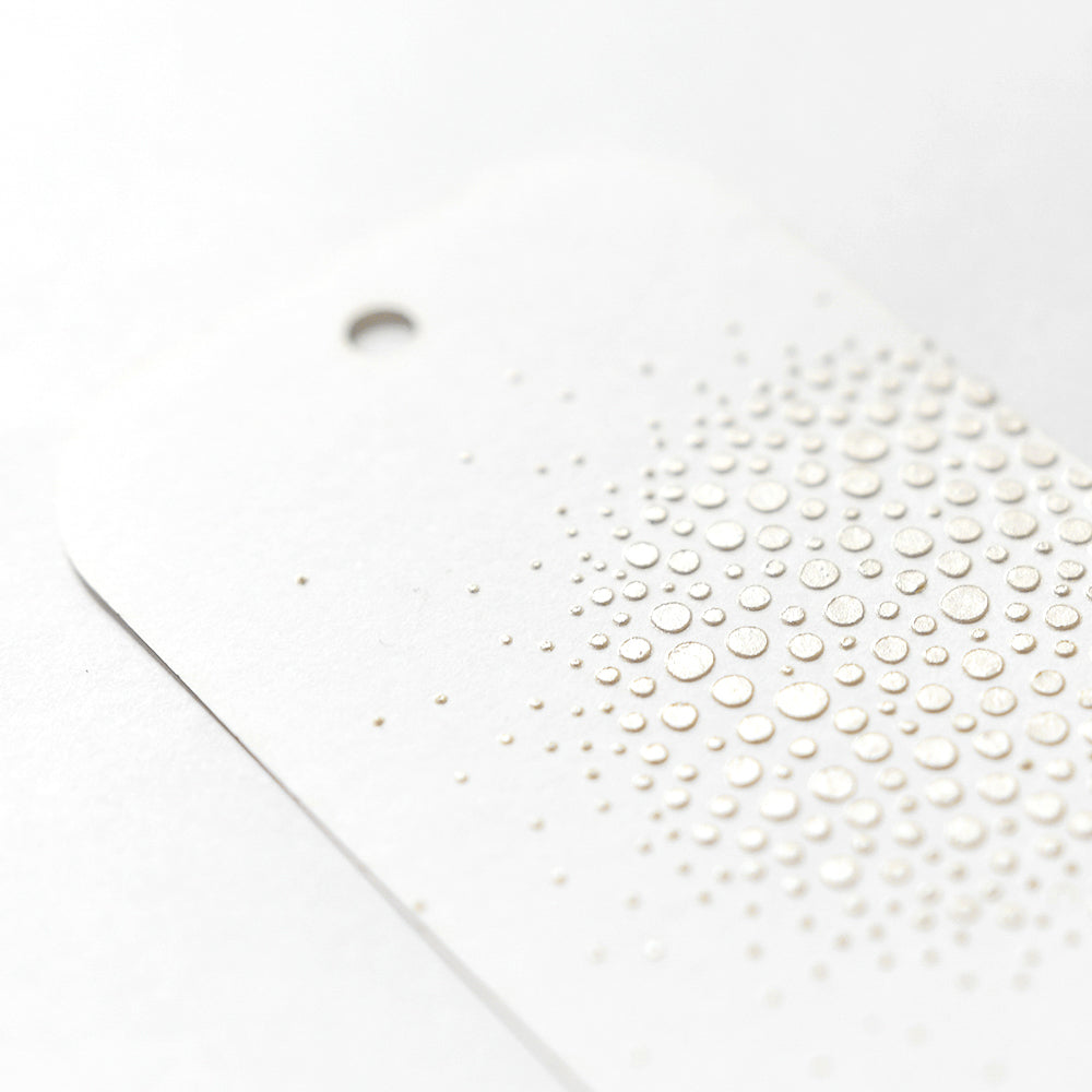 Weiße Karte von The Crafters Workshop mit einem geprägten Regentropfenmuster, das mit Modellierpaste erstellt wurde, und einem kleinen Loch oben links - ideal für Mixed-Media-Projekte.