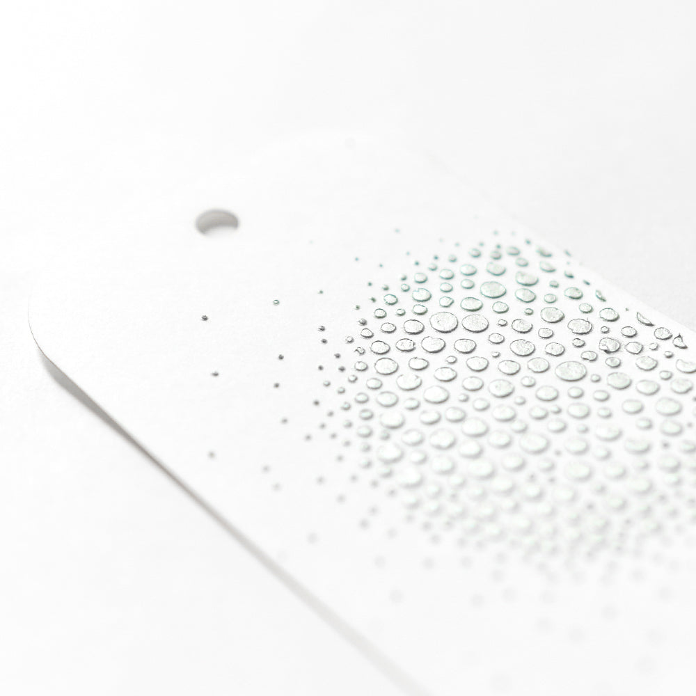 Ein weißer Anhänger von The Crafters Workshop mit einem Loch und erhabenen, klaren, wasserähnlichen Tropfen - ideal für Mixed Media-, Stencil Butter- und Schablonenprojekte.