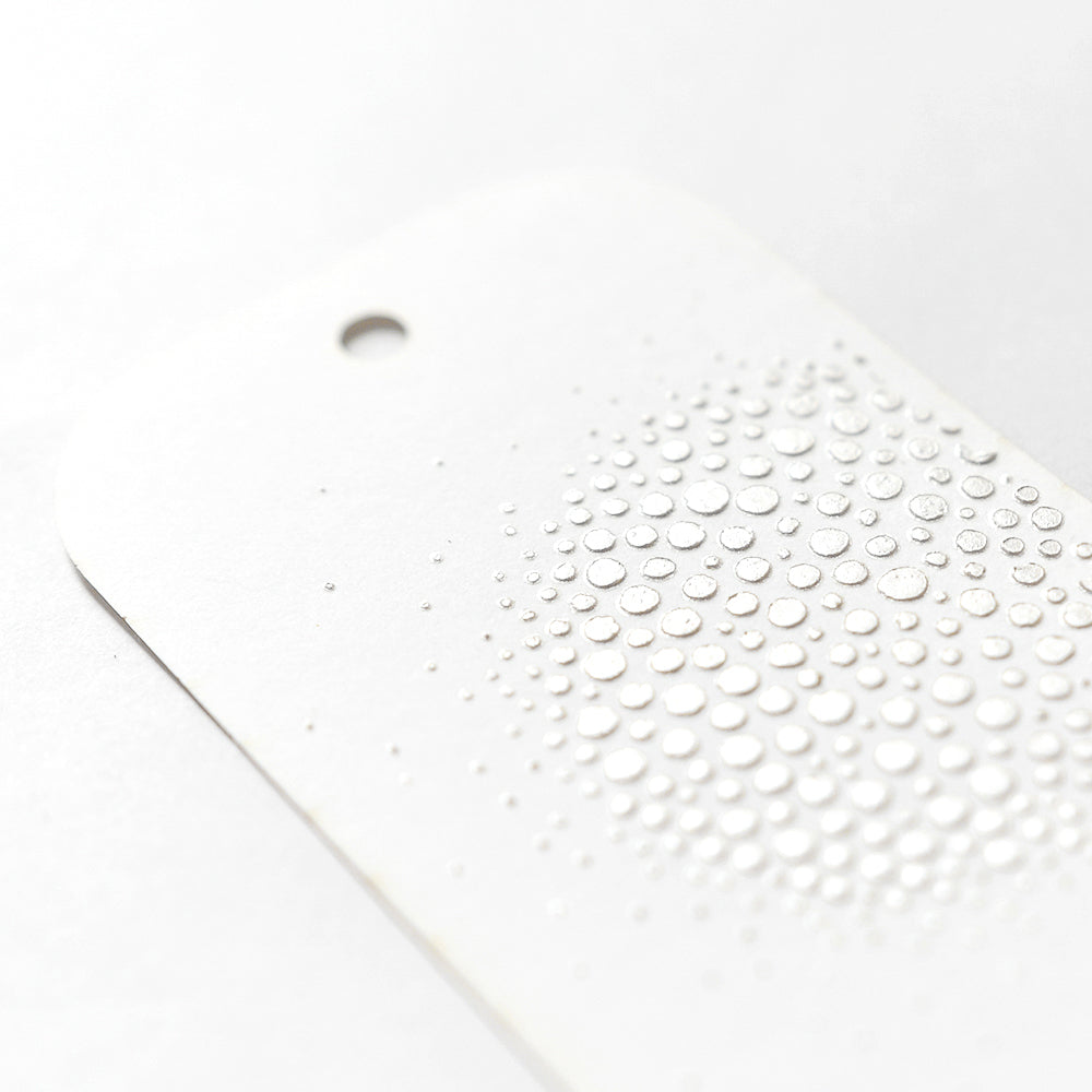 Der weiße Anhänger von Crafters Workshop hat ein Loch und erhabene, kreisförmige, geprägte Punkte in einem Farbverlaufsmuster - ideal, um mit Modellierpaste Texturen hinzuzufügen oder Details mit Mixed Media-Techniken hervorzuheben.