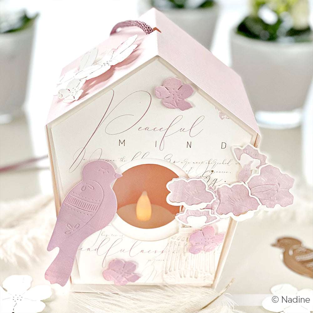 Rosa Papierlaterne von Alexandra Renke, geformt wie ein Vogelhaus mit Blumen- und Vogelausschnitten, hergestellt aus hochwertigem Designpapier und sanft beleuchtet von einer kleinen LED-Kerze im Inneren.