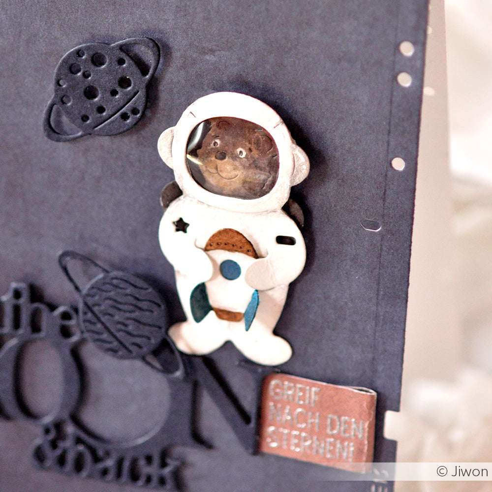 Eine handgefertigte Alexandra Renke Karte mit einer Motivstanze Astronautenbär im Astronautenanzug, Planeten, deutschem Text und Designpapiere Akzente auf dunklem Hintergrund.