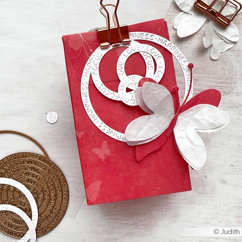 Rote Geschenkbox von Alexandra Renke mit weißem Motivstanze Schichtschmetterling und kreisrunden DieCut Systeme Ausschnitten, gesichert mit einer Kupferklammer und gefertigt aus hochwertigen Designpapieren auf hellem Grund.
