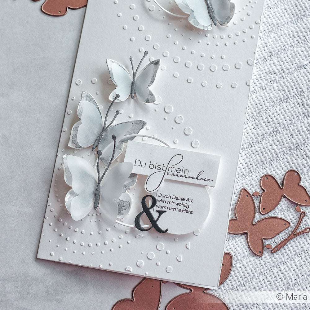 Handgefertigte Karte mit Schmetterlingen aus Schichtpapier, hergestellt mit Alexandra Renke Motivstanze Schichtschmetterling Dies, geprägten Punkten und deutschem Text, dargestellt auf einer strukturierten Oberfläche.