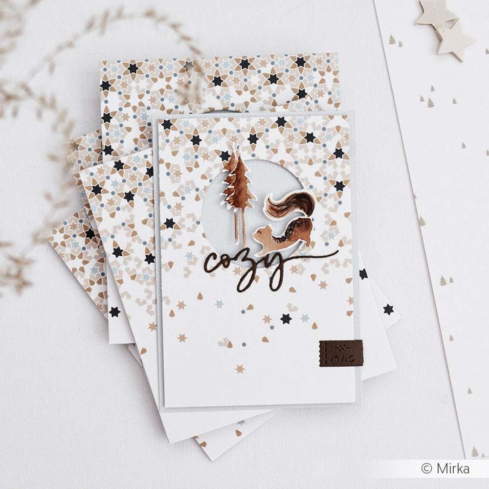 Ein Stapel sternförmiger Grußkarten von Alexandra Renke aus hochwertigen Designpapieren mit einem ausgeschnittenen Baum, der Motivstanze Eichhörnchen und dem Wort "gemütlich" in eleganter Schrift.
