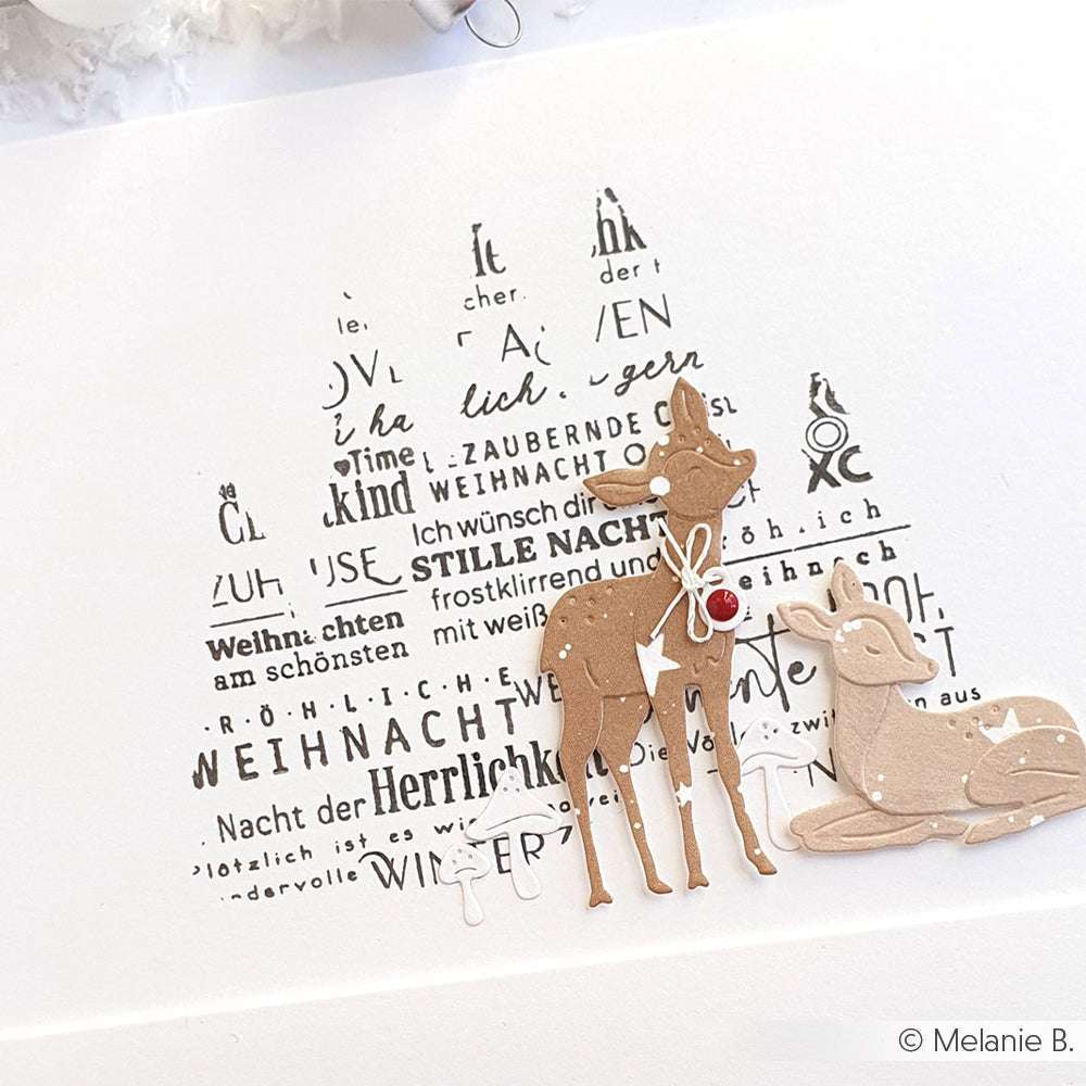 Zwei mit Alexandra Renke DieCut Systeme gestaltete Papierhirsche stehen vor einer Weihnachtsbaumform aus deutschen Weihnachtswörtern auf weißem Hintergrund.