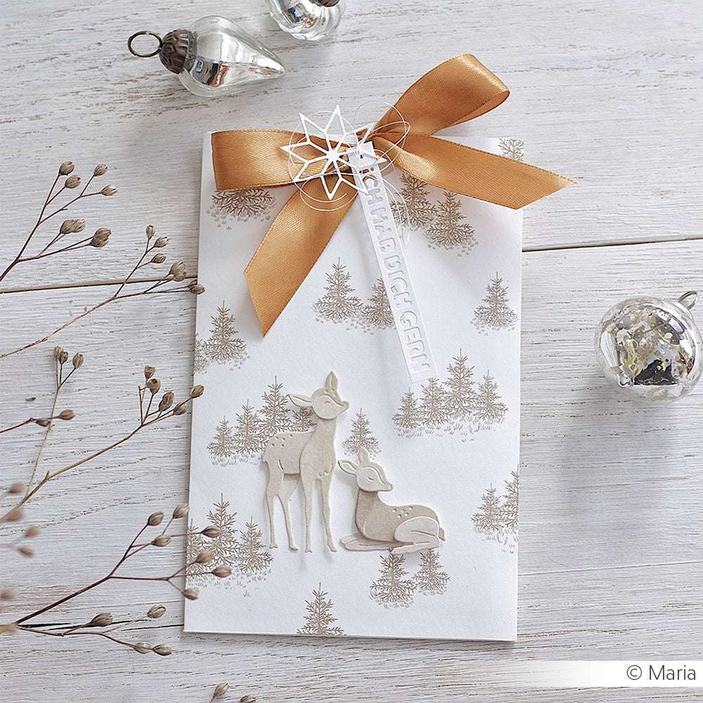 Weißer Umschlag mit goldenem Band, Waldmotiv und zwei Hirschen aus der Alexandra Renke Motivstanze Rehkitz, umgeben von weihnachtlichen Ornamenten und elegantem Designpapier.