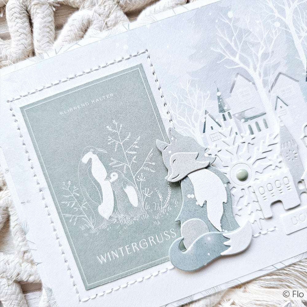Winterliche Grußkarte von Alexandra Renke mit einem Fuchs, Schneeflocken und einem verschneiten Dorf in sanften Pastellfarben, hergestellt mit der Motivstanze Fuchs für bezaubernde Details und kompatibel mit den meisten DieCut Systemen.
