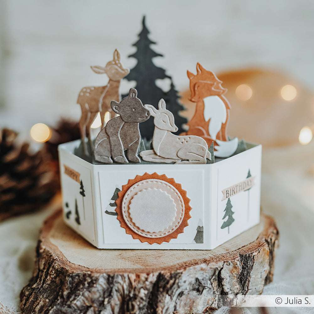 Sechseckige Geburtstagskarte von Alexandra Renke mit Waldtieren, Bäumen und geschichteten Designpapieren, die auf einer Holzscheibe präsentiert werden.