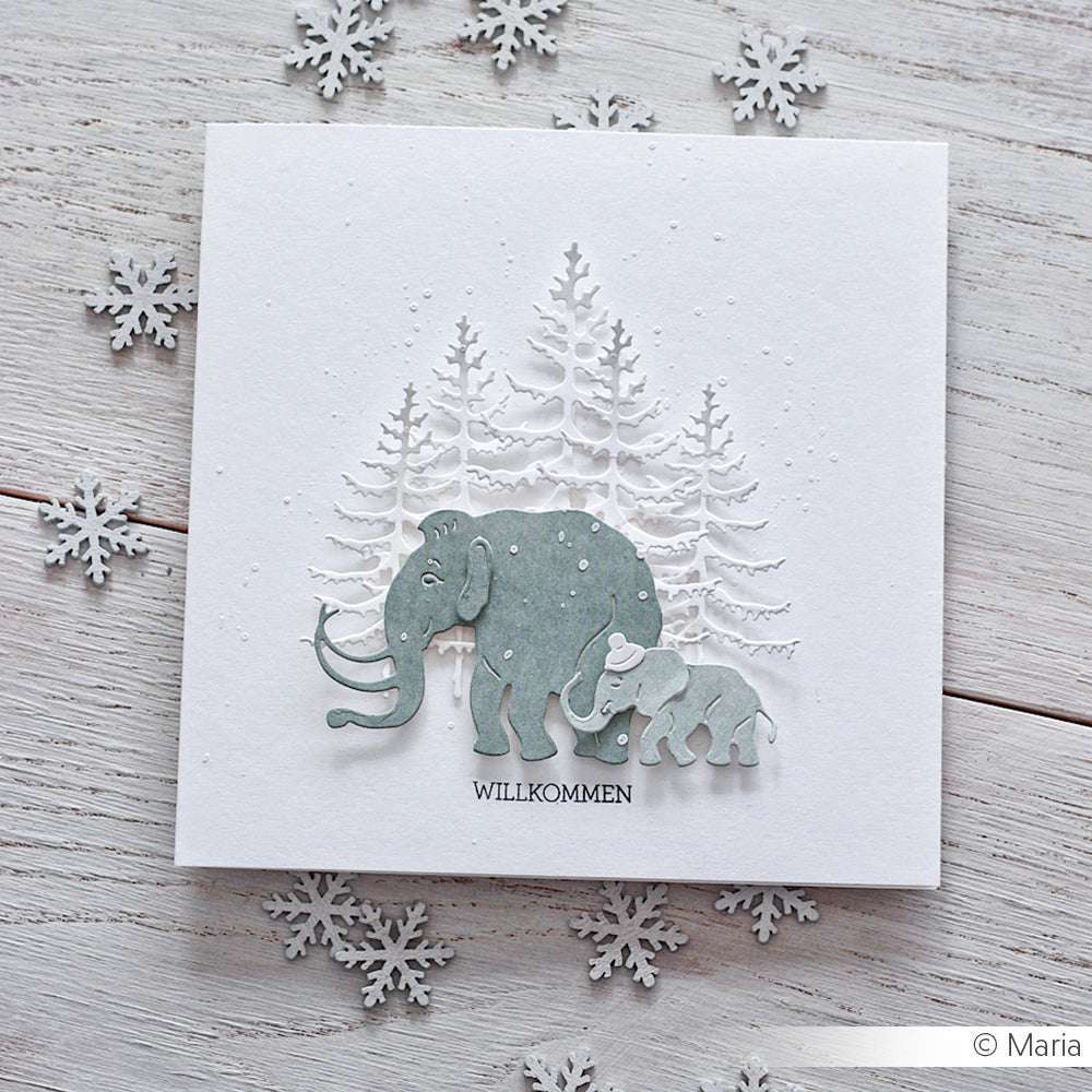 Handgemachte Karte von Alexandra Renke mit zwei Elefanten (Stanze Mammut Familie), verschneiten Bäumen, dem Text "WILLKOMMEN" und umgeben von Schneeflocken, die mit DieCut Systemen ausgestanzt wurden.