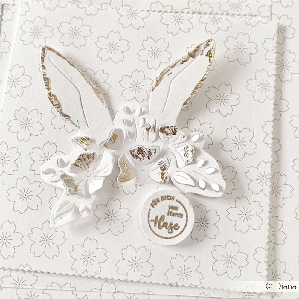 Weiß-goldene Karte mit Hasenohren und floralen Akzenten von Alexandra Renke, hergestellt mit DieCut Systemen und Designpapieren, enthält einen runden Anhänger mit der Aufschrift "Sei mutig, du hast Hase".