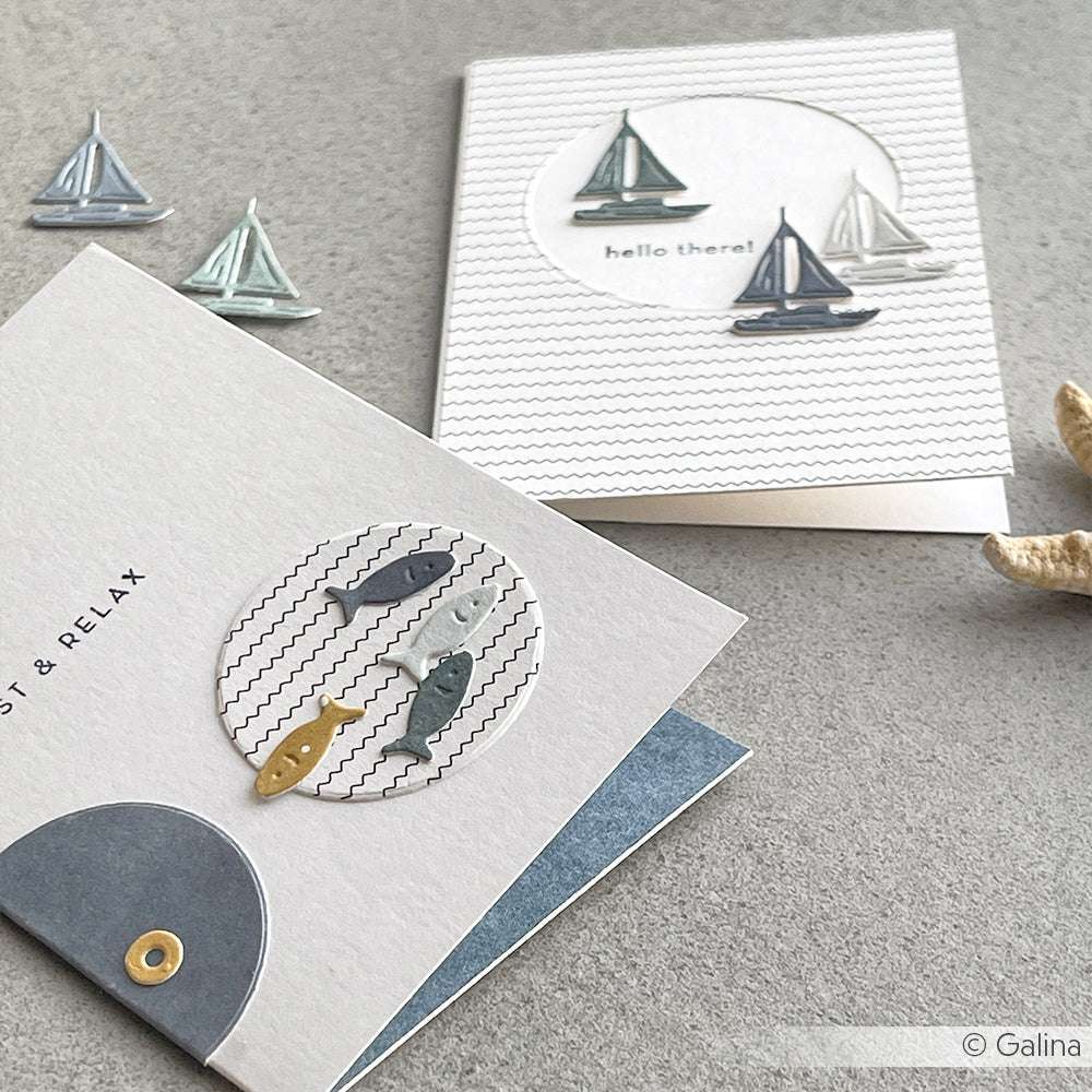 Zwei maritime Grußkarten von Alexandra Renke, hergestellt mit Stanzformen und dem Motivstanze Katzen-Angler Set, zeigen charmante Fisch- und Segelbootmotive auf einer hellgrauen Oberfläche.