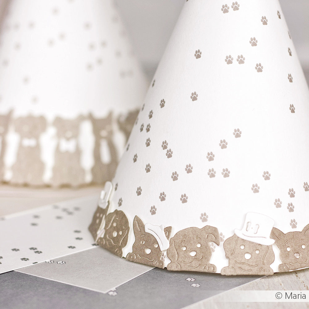 Nahaufnahme eines weißen Partyhuts mit Pfotenabdrücken und Cartoon-Tieren in Hüten - ideal für die individuelle Gestaltung mit Alexandra Renke Designpapieren oder DieCut Systemen für einen verspielten, einzigartigen Touch.