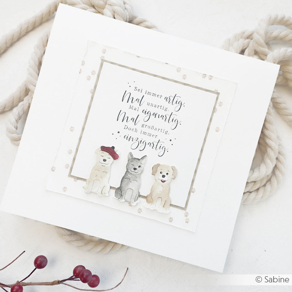 Eine Karte mit drei illustrierten Hunden und deutschem Text, hergestellt mit Alexandra Renke Motivstanze Schmucke Hunde Dies, ruht auf einer weißen Oberfläche, die mit Seil und Beeren verziert ist.
