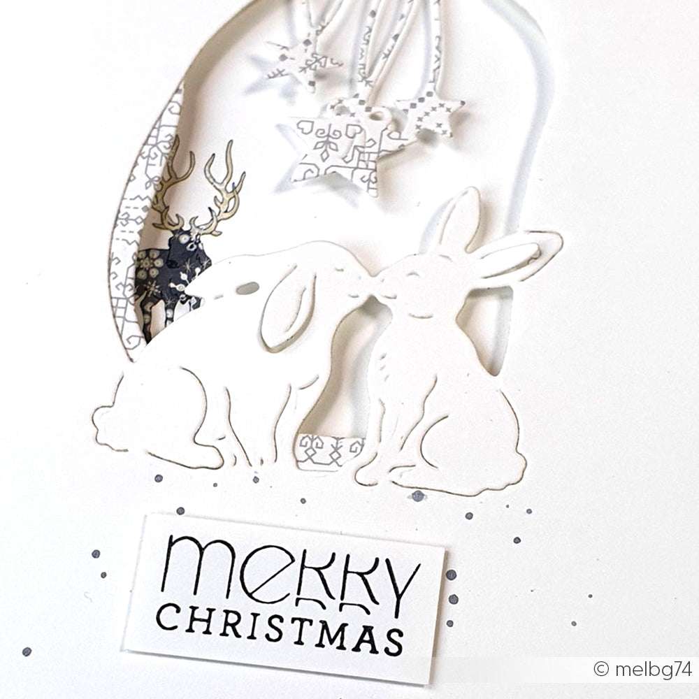 Zwei weiße Hasen kuscheln sich unter Sternen und einem Frohe-Weihnachten-Zeichen auf einer festlichen Karte, die mit Alexandra Renke Designpapieren und Motivstanze Hasen Pärchen DieCut Systeme für einen charmanten weihnachtlichen Touch gestaltet wurde.