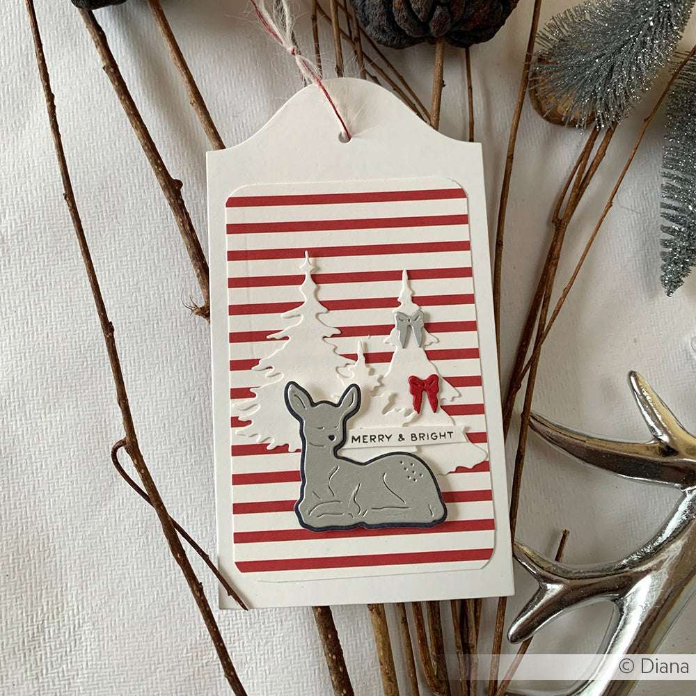 Eine Weihnachtskarte von Alexandra Renke mit roten Streifen, einem mit Motivstanze Rehkitz gestanzten grauen Reh, weißen Bäumen und einem "Merry & Bright"-Etikett auf hochwertigen Designpapieren.