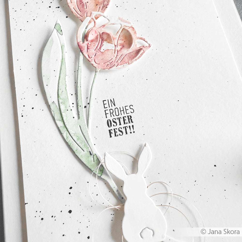 Osterkarte mit rosafarbenen Tulpen, einem weißen Hasen und "Ein frohes Osterfest!" auf weißem Untergrund, gestaltet mit Alexandra Renkes Motivstanze Hoppel Trio für charmante PAPPcut®ies-Details.