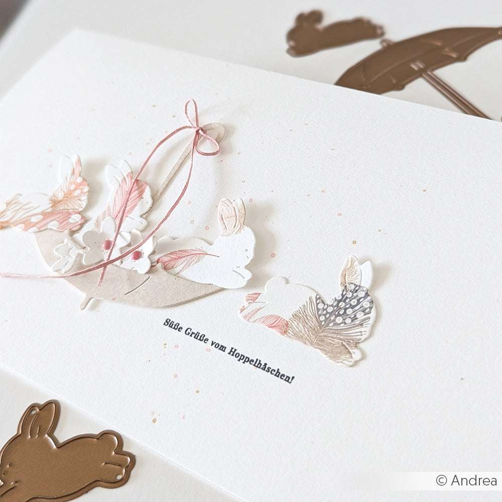 Handgefertigte Karte von Alexandra Renke mit pastellfarbenen Häschen, Blumen und einer rosa Schleife, die mit PAPPcut®ies hergestellt wurde. Enthält den Text: Süße Grüße vom Hoppelbäschen!.