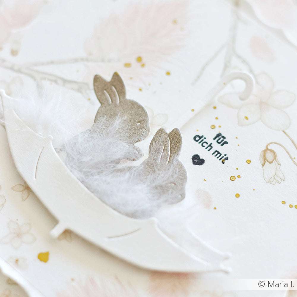 Papierhasen mit flauschigen Schwänzen, hergestellt mit Alexandra Renke PAPPcut®ies Deep Edge Motivstanzen, sitzen in einem weißen Papierschirm mit "für dich mit" im Hintergrund.