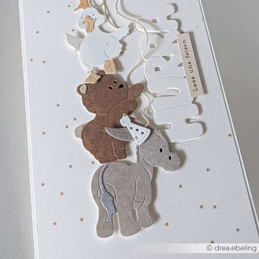 Gestapelte Tierausschnitte - eine Ente, ein Bär und Alexandra Renke PAPPcut®ies Kuschel-Esel - schmücken eine weiße Karte mit kleinen Sternen und dem Wort "Hurra!".