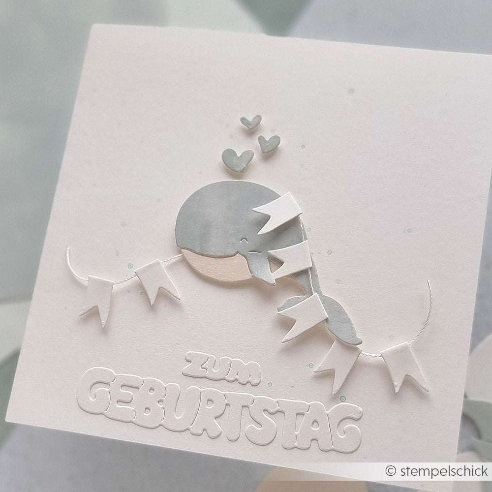 Liebenswerter Grauwal mit Herzen und einem Spruchband, das "Zum Geburtstag" auf einer weißen Geburtstagskarte zeigt. Gefertigt mit der Motivstanze Fröhlicher Wal von Alexandra Renke für zusätzlichen Charme.