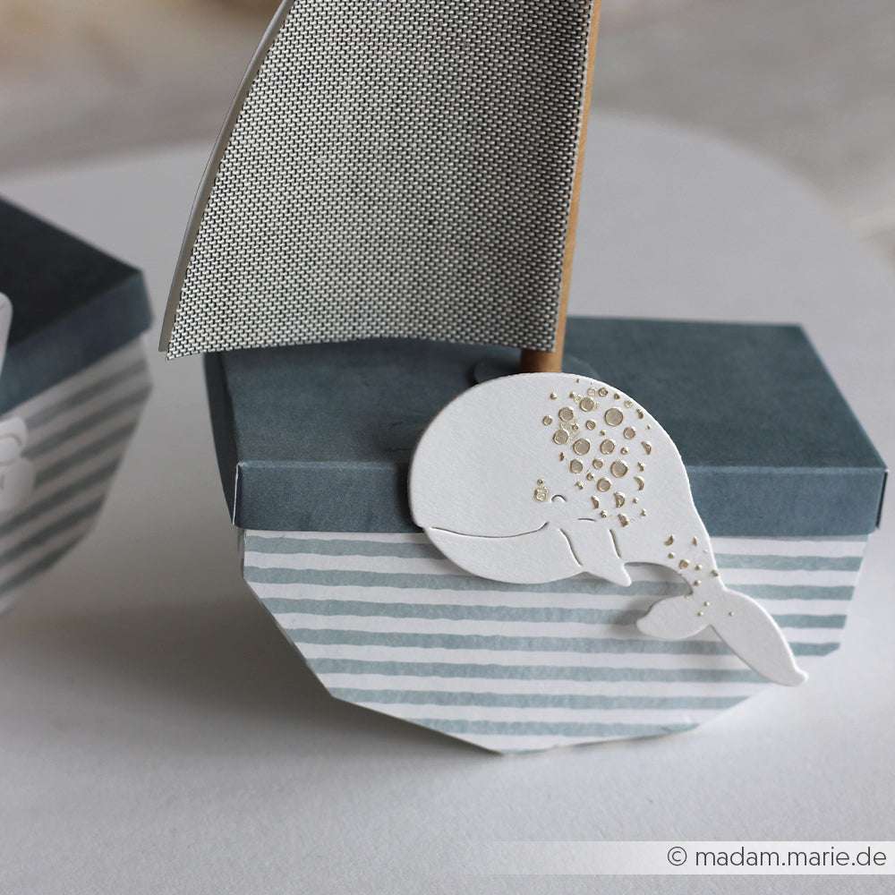 Eine kleine blaue Papierschachtel mit gestreiftem Segel und weißem Wal, hergestellt mit der Alexandra Renke PAPPcut®ies Deep Edge Motivstanze Fröhlicher Wal.