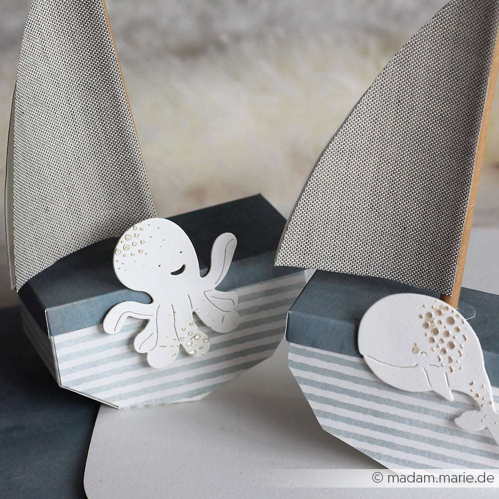 Zwei kleine PAPPcut®ies-Papierschachteln in Form eines Segelboots von Alexandra Renke, eine mit einem Motivstanze Oktopus und die andere mit einem charmanten Wal, sind eine entzückende Dekoration.