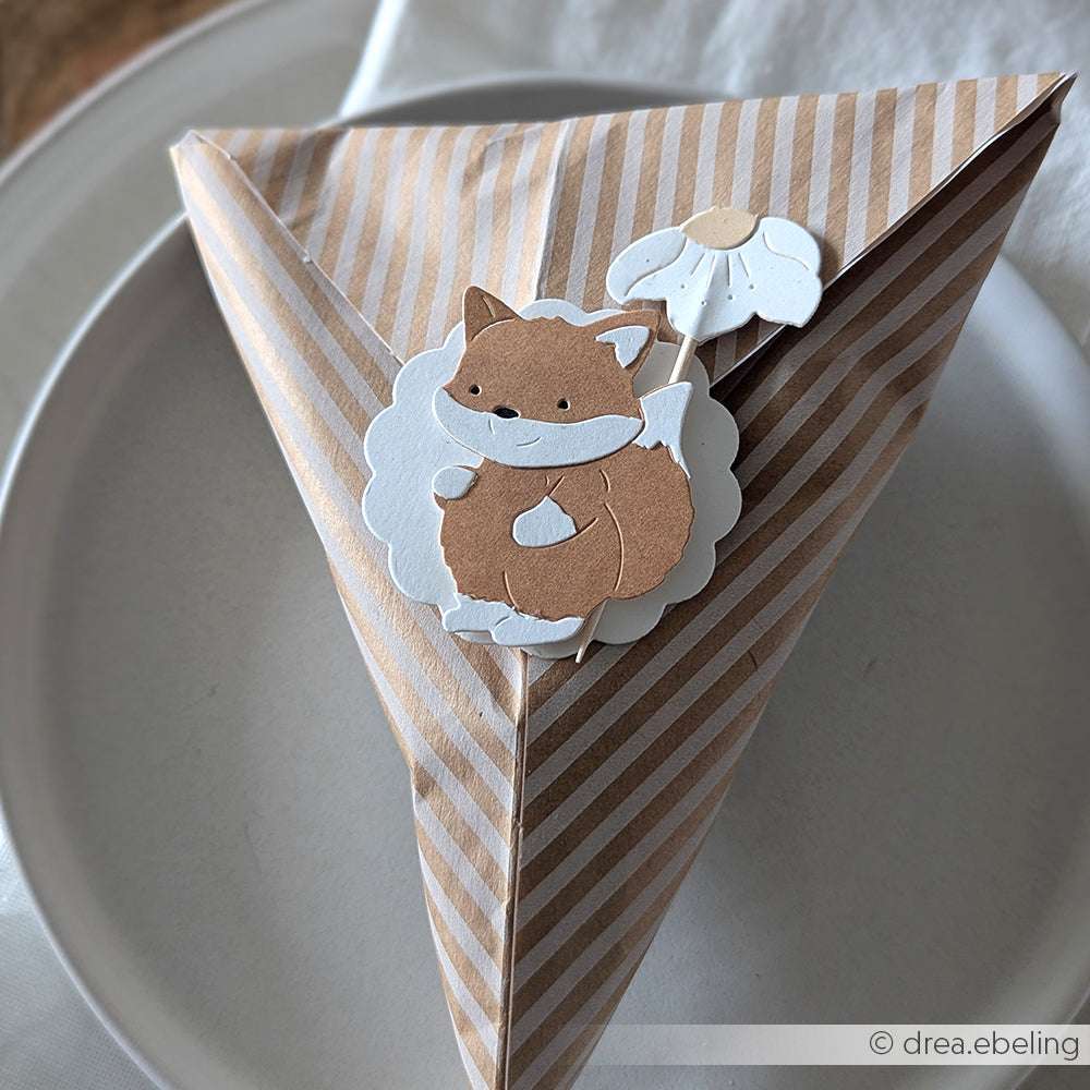 Eine gestreifte dreieckige Geschenkschachtel mit einem niedlichen Fuchs und einer weißen Blume, die mit Alexandra Renke's Deep Edge Motivstanzen hergestellt wurde und ein charmantes Finish bietet.