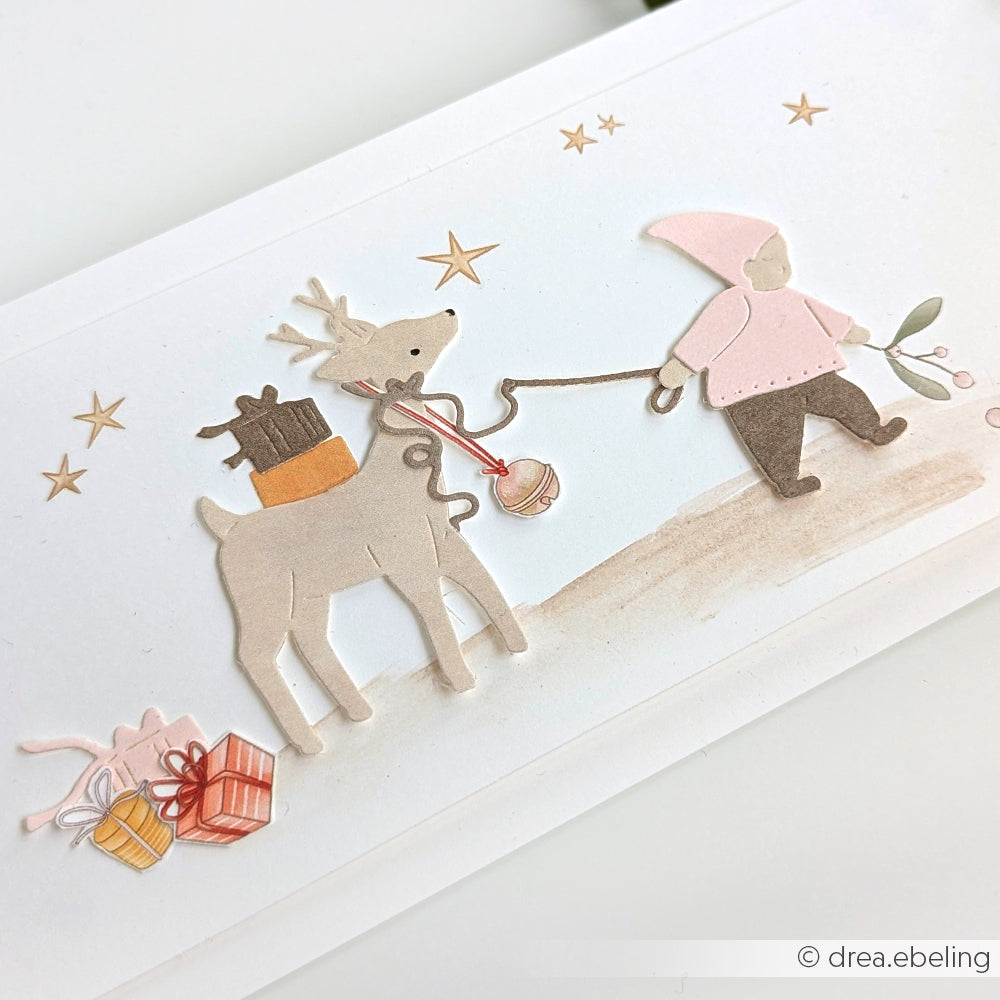 Ein Gnom führt ein Rentier, das Geschenke trägt; Sterne und Geschenke aus Alexandra Renke Designpapieren liegen auf dem Boden verstreut.