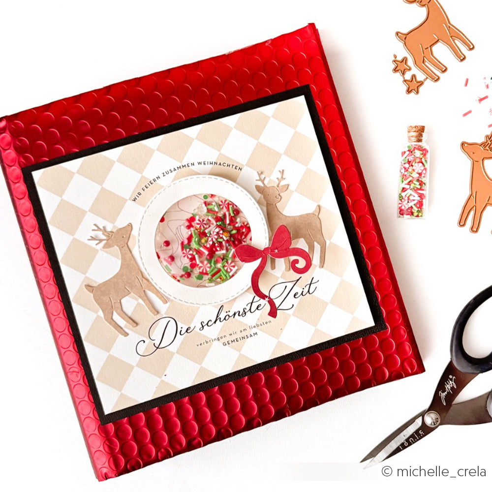 Rote Luftpolsterversandtasche mit einer Weihnachtskarte mit Rentieren, einer Schleife und festlichen Streuseln aus DieCut Systemen und leuchtenden Designpapieren von Alexandra Renke für zusätzliche Weihnachtsstimmung.