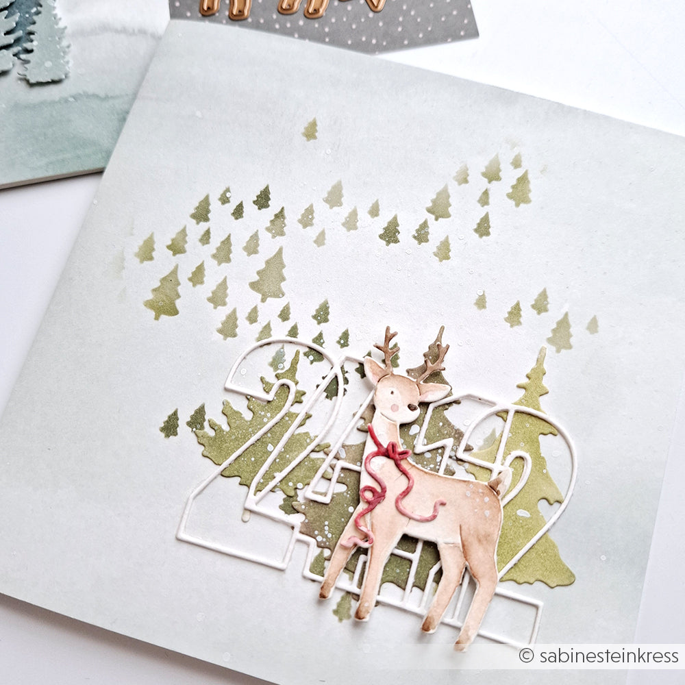 Handgefertigte Karte von Alexandra Renke mit einem Hirsch, Tannenbäumen und 2024 auf einem zartgrünen Hintergrund mit Baumsilhouetten, hergestellt mit Motivstanzen aus der Kollektion Tierische Sternfreunde Stanzsysteme.