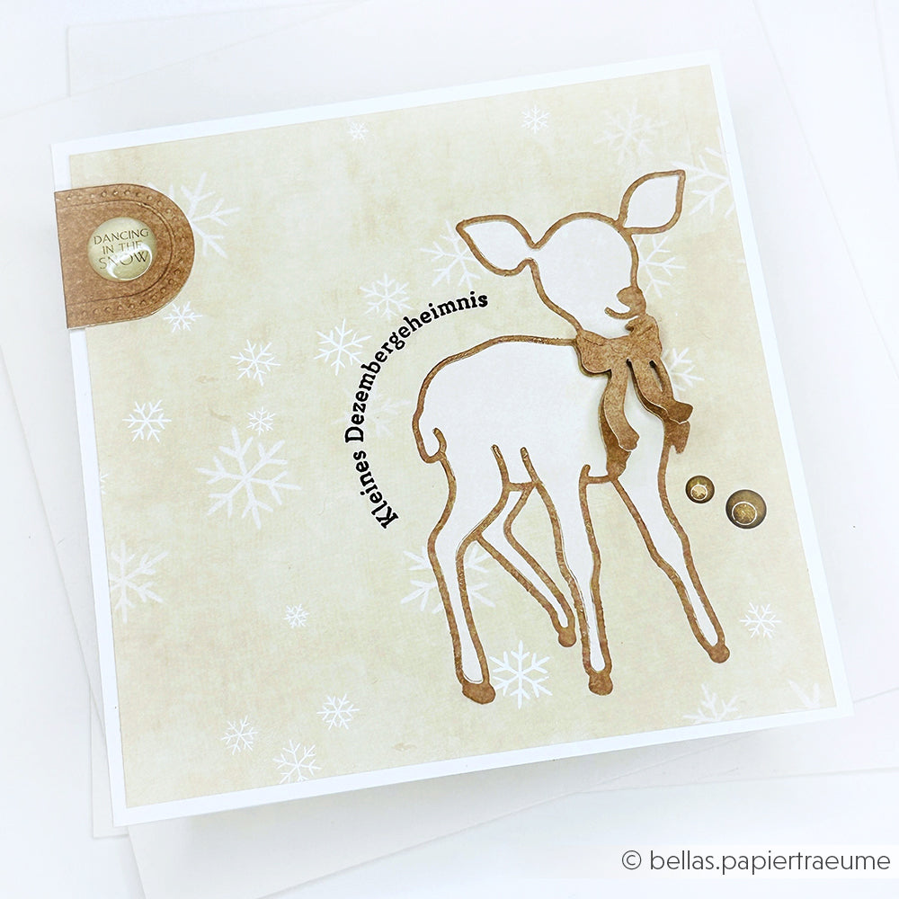 Handgemachte Karte von Alexandra Renke mit einem braun umrandeten Reh aus Motivstanze Reh, einer roten Schleife, Schneeflocken und deutschem Text auf beigem Designpapier.