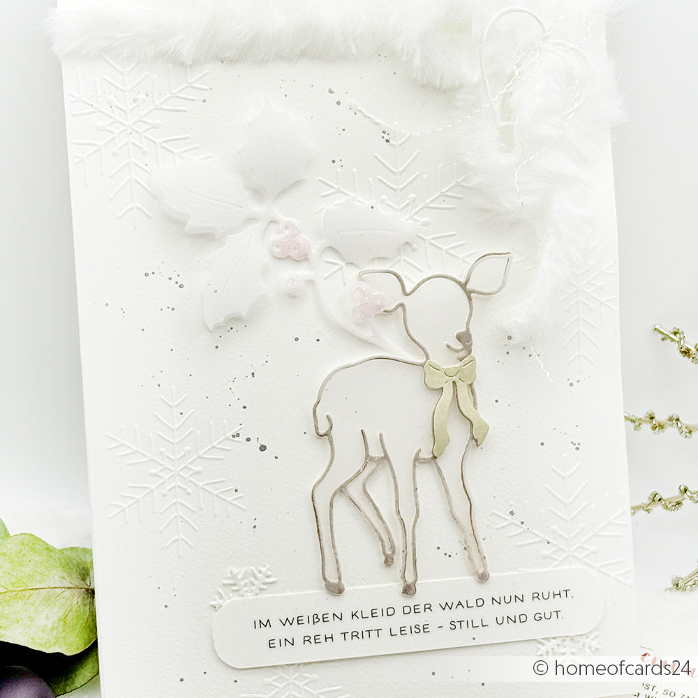 Handgemachte weiße Karte von Alexandra Renke, erstellt mit Dies und Stanzsystemen. Mit einer Motivstanze Zauberhaftes Reh, Schneeflocken, Stechpalmenblättern und einem deutschen Wintergedicht am unteren Rand.